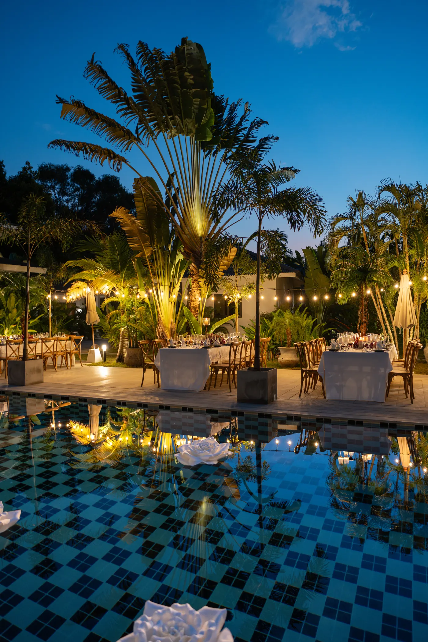 Wedding reception dinner tables beside a lit pool at twilight